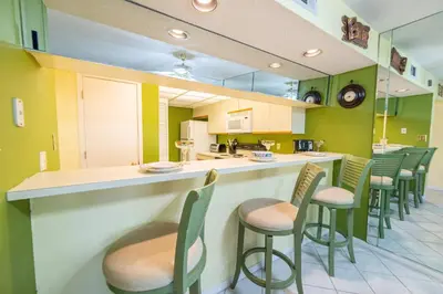 a kitchen with green walls and a bar with chairs at Edgewater Villa 3005 'Paradise Palms' in Panama City Beach