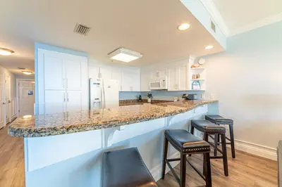 a kitchen with white cabinets and a counter with stools at Boardwalk 1409 'Emerald Ray' in Panama City Beach