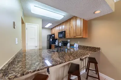 a kitchen with a granite counter top and wooden cabinets at Edgewater Villa 1303 'Gone Gulf'N' in Panama City Beach