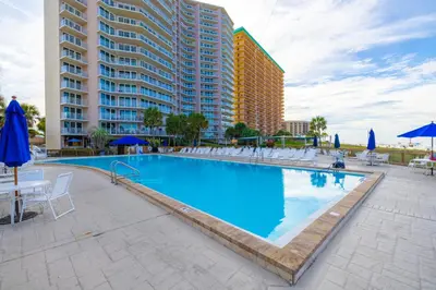 a large swimming pool with chairs and blue umbrellas at Dunes of Panama E1703 'After-Dune Delight' in Panama City Beach