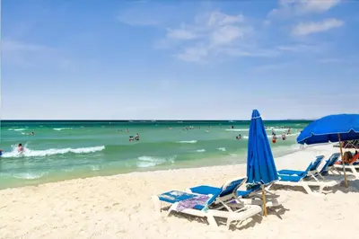 a beach with chairs and umbrellas and the ocean at Sunbird Resort Ground Floor Gem with Ocean Views! Free Beach Chairs and Umbrella! by Dolce Vita Getaways PCB in Panama City Beach
