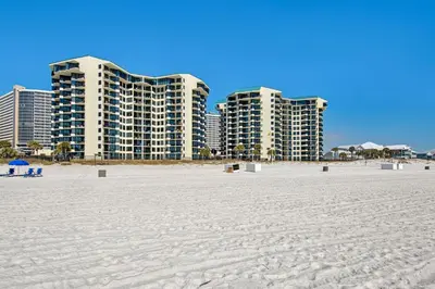 a beach with two tall buildings in the background at Sunbird Resort Ground Floor Gem with Ocean Views! Free Beach Chairs and Umbrella! by Dolce Vita Getaways PCB in Panama City Beach