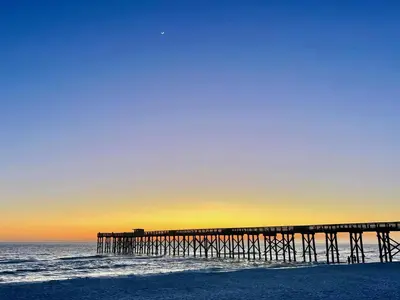 a pier on the ocean with the sun setting at Sunbird Resort Ground Floor Gem with Ocean Views! Free Beach Chairs and Umbrella! by Dolce Vita Getaways PCB in Panama City Beach