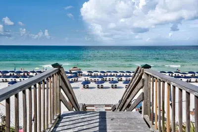 a staircase leading to a beach with chairs and umbrellas at Wine Down 30A in Seacrest
