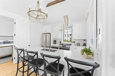 a kitchen with white cabinets and a white island with black chairs at Abba Carriage House in Rosemary Beach