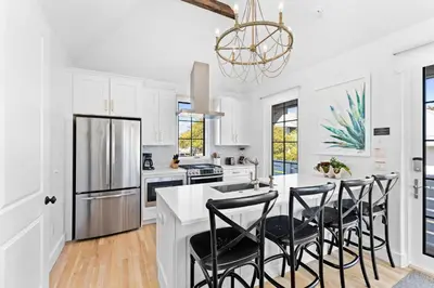 a kitchen with white cabinets and a white island with black chairs at Abba Carriage House in Rosemary Beach