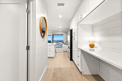 a kitchen with white cabinets and a hallway with a mirror at Latitude 29 Unit 21 in Panama City Beach