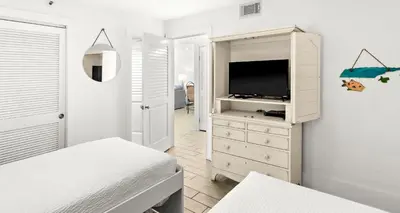 a white bedroom with a tv and a dresser at One Seagrove Place 1302 in Santa Rosa Beach
