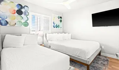 a white bedroom with two beds and a flat screen tv at One Seagrove Place 1008 in Santa Rosa Beach