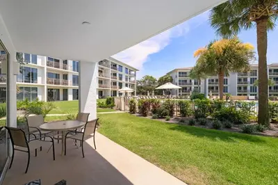 a patio with a table and chairs and a lawn with palm trees at High Pointe Resort 131 in Inlet Beach