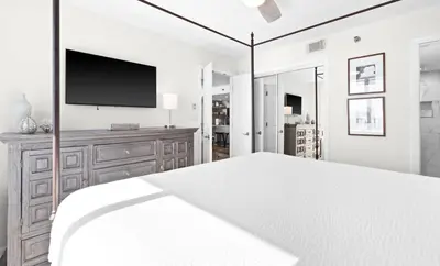 a white bedroom with a bed and a flat screen tv at One Seagrove Place 0406 in Santa Rosa Beach