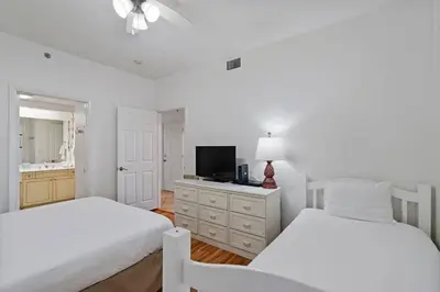 a white bedroom with two beds and a television at High Pointe Resort E26 in Inlet Beach