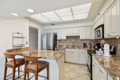 a kitchen with white cabinets and a island with bar stools at High Pointe Resort E26 in Inlet Beach