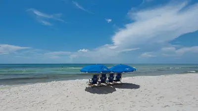 two chairs and two blue umbrellas on a beach at Mistral 12 in Seacrest
