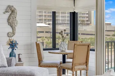 a dining room with a table and chairs and windows at Newly Completely Renovated Beach Condo at Sunbird Resort! Free Beach Chair and Umbrella Service! by Dolce Vita Getaways! in Panama City Beach