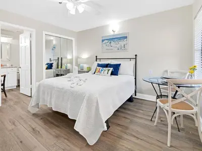 a white bedroom with a bed and a table at Charming Beach Studio With Pool & Sauna in Panama City Beach