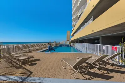 a swimming pool next to a building with chairs at Emerald Isle 1504 in Panama City Beach