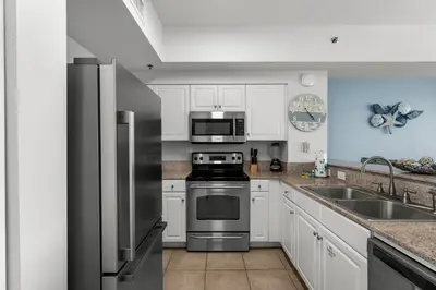 a kitchen with stainless steel appliances and white cabinets at Stylish 1BD Beachfront Condo with Amenities Galore! by Dolce Vita Getaways! in Panama City Beach