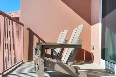 a chair sitting on a balcony next to a building at Stylish 1BD Beachfront Condo with Amenities Galore! by Dolce Vita Getaways! in Panama City Beach