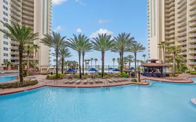 a large swimming pool with palm trees and buildings at Stylish 1BD Beachfront Condo with Amenities Galore! by Dolce Vita Getaways! in Panama City Beach