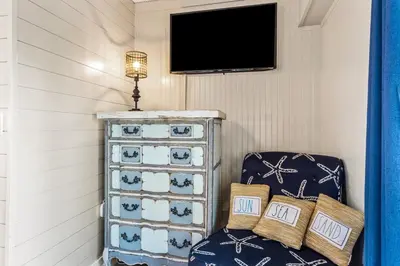 a room with a chair and a dresser with a tv at K and J Panama City Beach in Panama City Beach