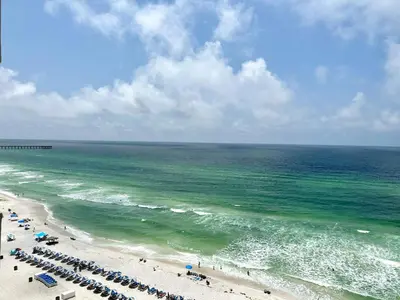 a beach with chairs and umbrellas and the ocean at Tidewater 1005 in Panama City Beach