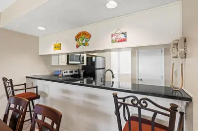 a kitchen with a black counter top and chairs at Edgewater Golf Villa 605 in Panama City Beach