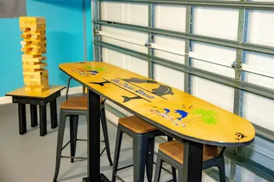 a wooden surfboard sitting on top of a table with stools at Tropical Oasis, Tiki Bar, Pool, Mini Golf, Hot Tub in Panama City Beach