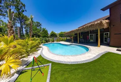 a swimming pool in a yard next to a house at Tropical Oasis, Tiki Bar, Pool, Mini Golf, Hot Tub in Panama City Beach