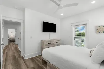 a white bedroom with a bed and a flat screen tv at Cottages at Eastern Lake by Panhandle Getaways in Santa Rosa Beach