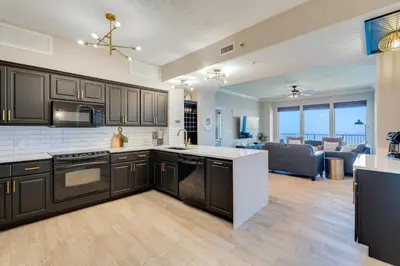 a kitchen with black cabinets and a living room at Newly Renovated Luxury OCEAN FRONT Condo! Top Floor Condo with PENTHOUSE OCEAN VIEWS! in Panama City Beach