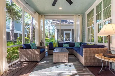 a screened in porch with a blue couch and chairs at Plimsoll Retreat at Watersound West Beach in Santa Rosa Beach