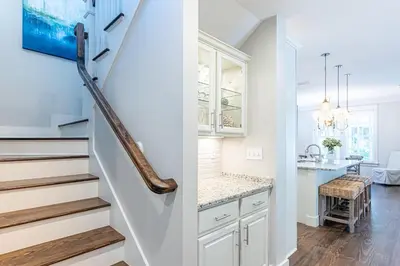 a kitchen with white cabinets and a staircase with a table at Plimsoll Retreat at Watersound West Beach in Santa Rosa Beach
