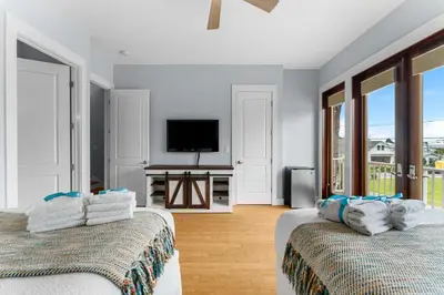 two beds in a room with a tv and windows at Beach Bay Getaway! Bayfront 4BR 4BA House Sleeps 12 Private pool Boat dock in Panama City Beach