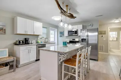 a kitchen with white cabinets and a kitchen island with bar stools at Sea Breeze House- 3 bd 2 ba 5 min walk to beach in Panama City Beach