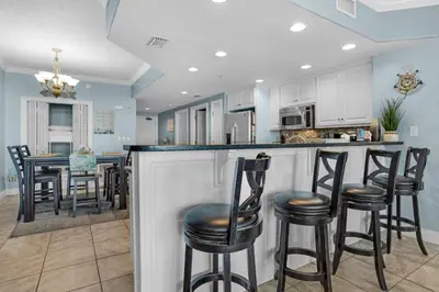 a kitchen with white cabinets and black bar stools at Treasure Island 1904 in Panama City Beach