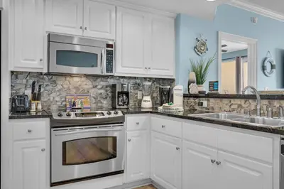 a kitchen with white cabinets and a sink and a microwave at Treasure Island 1904 in Panama City Beach