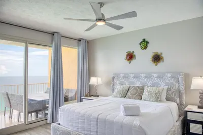 a bedroom with a bed with a ceiling fan and a balcony at Treasure Island 1811 in Panama City Beach