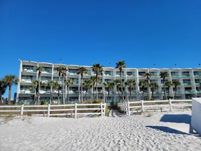 a building on the beach with palm trees and a fence at Casa Loma Panama City Beach - Beachfront in Panama City Beach