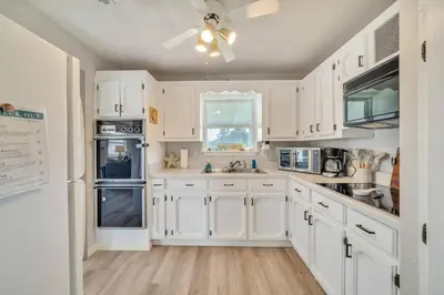 a white kitchen with white cabinets and a ceiling fan at Nearby Beach l Friends & Family l Pet-Friendly in Panama City Beach