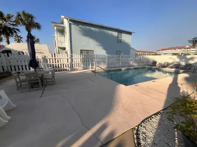 a patio with a pool and a table and an umbrella at Cozy Two-Bedroom Cottage-5min walk to beach! in Panama City Beach