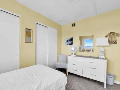 a bedroom with a bed and a dresser with a lamp and a chair at Pinnacle Port A-305 in Panama City Beach