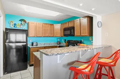 a kitchen with a black refrigerator and two orange bar stools at Pelican Walk 404 in Panama City Beach