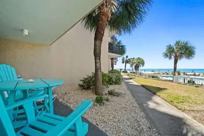 a patio with blue chairs and a table and palm trees at Pelican Walk 112 in Panama City Beach