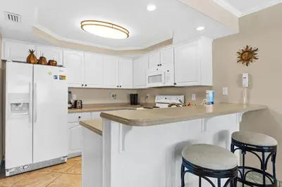 a kitchen with white cabinets and a counter with stools at Pelican Walk 402 in Panama City Beach