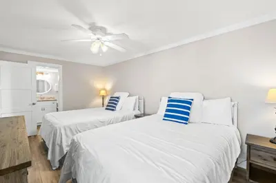 two beds in a white room with a ceiling fan at Pelican Walk 501 in Panama City Beach