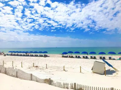 a beach with umbrellas and chairs and the ocean at Pelican Walk 502 in Panama City Beach