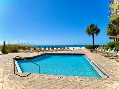 a swimming pool with chairs and the ocean in the background at Pelican Walk 110 in Panama City Beach