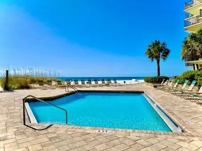 a swimming pool with chairs and the ocean in the background at Pelican Walk 710 in Panama City Beach