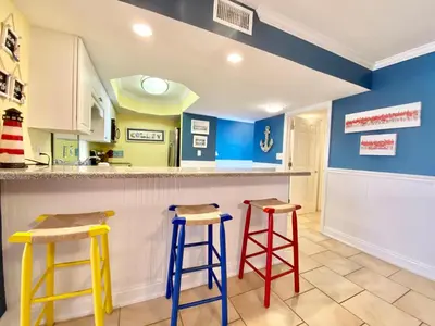 a kitchen with yellow and blue walls and stools at Gulfgate 304 in Panama City Beach